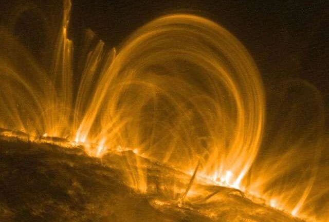 Por que a coroa solar é tão quente? Estendendo-se acima da fotosfera ou da superfície visível do Sol, a coroa solar não pode ser facilmente vista da Terra, mas sabe-se que ela é centenas de vezes mais quente do que a própria fotosfera. Há muito procura-se entender melhor a fonte do calor da coroa e seus campos magnéticos, que lançam anéis coronais de plasma solar, acima da fotosfera. Observações detalhadas desses fenômenos foram feitas pelo satélite TRACE. Registadas em luz ultravioleta extrema, esta e outras imagens do TRACE indicam que ocorre um aquecimento significativo na parte inferior da coroa, perto das bases dos anéis, à medida que emergem e regressam à superfície solar. Os anéis coronais desta imagem abrangem 30 ou mais vezes o diâmetro do planeta Terra