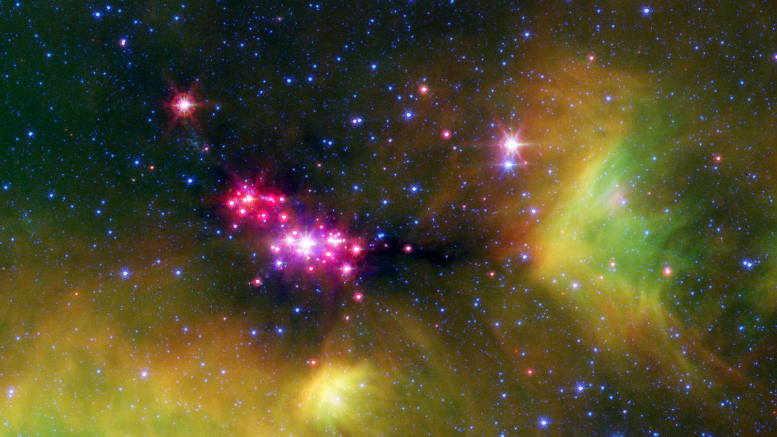 Estrelas em sua infância brilham gloriosamente nesta imagem, feita em infravermelho, da região de formação estelar de Serpens, registrada pelo Telescópio Espacial Spitzer, da Nasa. Os pontos rosa-avermelhados são estrelas bebês profundamente incrustadas na nuvem cósmica de gás e poeira que entrou em colapso. Um disco empoeirado de detritos cósmicos, ou “disco protoplanetário”, que pode eventualmente formar planetas, rodeia as estrelas jovens. Fios verdes indicam a presença de moléculas ricas em carbono, chamadas hidrocarbonetos policíclicos aromáticos. As manchas azuis são estrelas de fundo, na Via Láctea. A região de formação estelar de Serpens está localizada a aproximadamente 848 anos-luz de distância, na Constelação de Serpens
