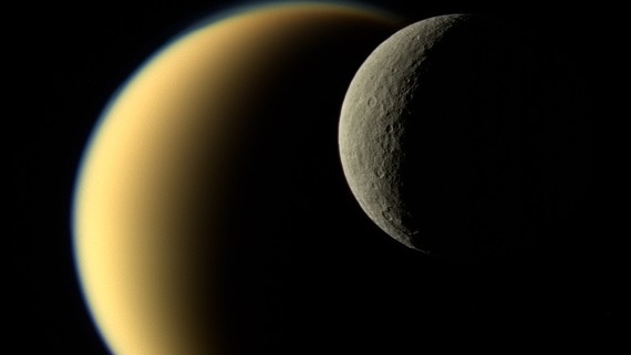 Nesta imagem, registrada em novembro de 2009, a lua gelada de Saturno, Reia, passa em frente de Titã, na visão da sonda Cassini, da NASA. Algumas das diferenças entre as duas grandes luas são facilmente notadas. Embora Reia seja um mundo sem ar e com muitas crateras, a atmosfera rica em nitrogênio de Titã é ainda mais espessa que a da Terra. A espaçonave Cassini encerrou sua missão em 15 de setembro de 2017