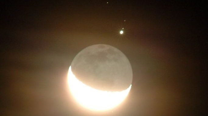 Esta imagem foi registrada em dezembro de 2004, no céu de Atmore, Alabama, EUA. Nela, a Lua Crescente é vista ao lado do que parece, à primeira vista, uma estrela. Na verdade, o que se vê é o brilhante Júpiter, o planeta gigante gasoso que reina no Sistema Solar. Visto através de nuvens finas, Júpiter aparece juntamente com dois de seus satélites naturais: Ganimedes e Calisto (de baixo para cima)