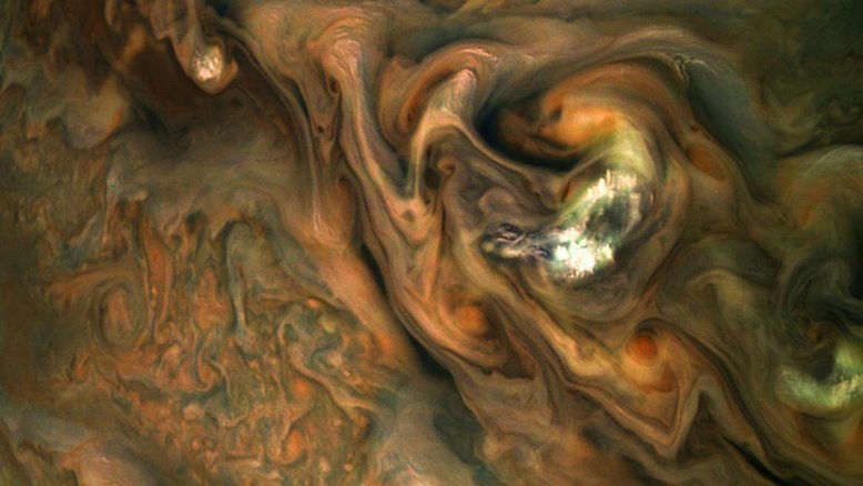 Esta imagem capturada pela sonda Juno, da NASA, mostra padrões coloridos e intrincados, em uma região de correntes de jato, no Hemisfério Norte de Júpiter, conhecida como “Jet N3”. Os topos das nuvens de Júpiter não formam uma superfície simples e plana. As faixas rodopiantes na atmosfera se estendem por até 3 mil quilômetros de profundidade. À direita do centro, uma mancha de nuvens brilhantes e de alta altitude se sobressai em relação à atmosfera circundante. A imagem é de maio de 2019 e, no momento em que o registro foi feito, a sonda estava a cerca de 9,7 mil quilômetros do topo das nuvens