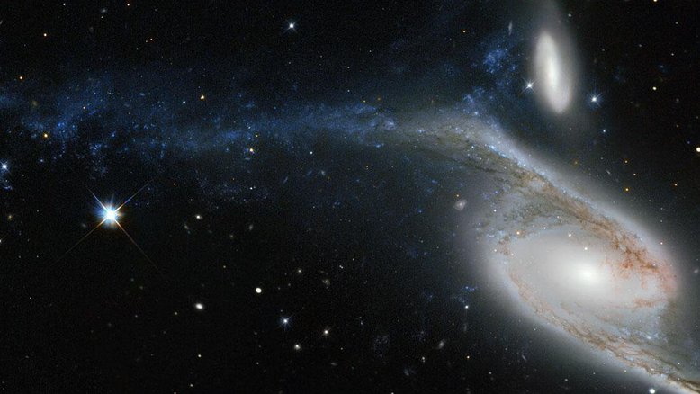 NGC 6872 é uma galáxia de formato incomum, localizada na direção da Constelação de Pavo (“O Pavão”). A sua deformação é resultado das interações com a galáxia menor, vista logo acima nesta imagem, cuja designação é IC 4970. Ambas ficam a cerca de 300 milhões de anos-luz de distância da Terra. De ponta a ponta, NGC 6872 mede mais de 500 mil anos-luz de diâmetro, tornando-a a segunda maior galáxia espiral descoberta até hoje. Para colocar isso em perspectiva, a nossa galáxia, a Via Láctea, mede entre 100 mil e 120 mil anos-luz de diâmetro, fazendo com que NGC 6872 tenha cerca de cinco vezes o seu tamanho