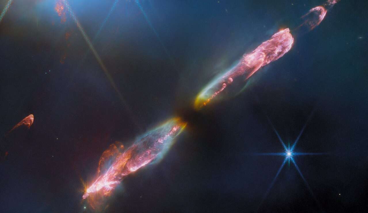 Nesta imagem do Telescópio Espacial James Webb, vê-se o objeto Herbig-Haro 211 (HH 211), um jato bipolar viajando pelo espaço interestelar em velocidades supersônicas. A cerca de mil anos-luz de distância da Terra, na direção da Constelação de Perseu, ele é um dos fluxos protoestelares mais jovens e mais próximos. Os objetos Herbig-Haro circundam estrelas recém-nascidas e são formados quando ventos estelares ou jatos de gás, expelidos por essas estrelas, formam ondas de choque que colidem com gás e poeira em alta velocidade. Esta imagem de HH 211 revela o fluxo externo de uma protoestrela de Classe 0, análoga infantil do nosso Sol, quando ele não tinha mais do que algumas dezenas de milhares de anos e apenas 8% de sua massa atual