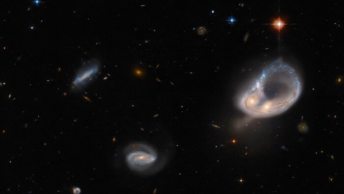 A fusão de galáxias Arp-Madore 417-391 rouba os holofotes nesta imagem do Telescópio Espacial Hubble. O catálogo Arp-Madore é uma coleção de galáxias particularmente peculiares, muitas delas que interagem sutilmente ou em colisões espetaculares. Arp-Madore 417-391, que fica a cerca de 670 milhões de anos-luz de distância, na Constelação de Eridanus, é uma dessas colisões galácticas. As duas galáxias foram distorcidas pela gravidade e torcidas num anel colossal, deixando os seus núcleos lado a lado