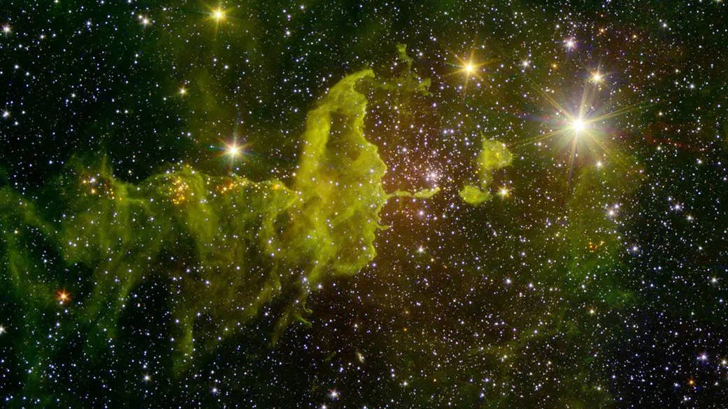 A nebulosa IC 417 está repleta de formação estelar, como pode ser visto nesta imagem feita em infravermelho. Localizado na Constelação de Auriga (“O Cocheiro”), IC 417 fica a cerca de 10 mil anos-luz de distância. Ela fica na parte externa da Via Láctea, quase exatamente na direção oposta ao centro galáctico. Um aglomerado de estrelas jovens, chamado de Stock 8, pode ser visto no centro e à direita. A luz deste aglomerado forma uma espécie de tigela nas nuvens de poeira próximas, vistas aqui como uma penugem verde. Ao longo da cauda sinuosa, no centro e à esquerda, agrupamentos que servem como fontes de luzes vermelhas também são estrelas jovens