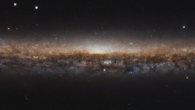 NGC 5907 é uma galáxia espiral, assim como a Via Láctea. Estendo-se por toda esta imagem como uma linha alongada de estrelas e poeira escura, seus belos braços espirais estão ocultos devido ao ângulo de visão a partir da Terra. Como a vemos de lado, é como se estivéssemos olhando para a borda de um prato. Por esse motivo, NGC 5907 também é conhecida como Galáxia da Lâmina da Faca, ficando a cerca de 50 milhões de anos-luz distância, na direção da boreal Constelação de Draco