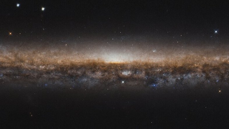 NGC 5907 é uma galáxia espiral, assim como a Via Láctea. Estendo-se por toda esta imagem como uma linha alongada de estrelas e poeira escura, seus belos braços espirais estão ocultos devido ao ângulo de visão a partir da Terra. Como a vemos de lado, é como se estivéssemos olhando para a borda de um prato. Por esse motivo, NGC 5907 também é conhecida como Galáxia da Lâmina da Faca, ficando a cerca de 50 milhões de anos-luz distância, na direção da boreal Constelação de Draco