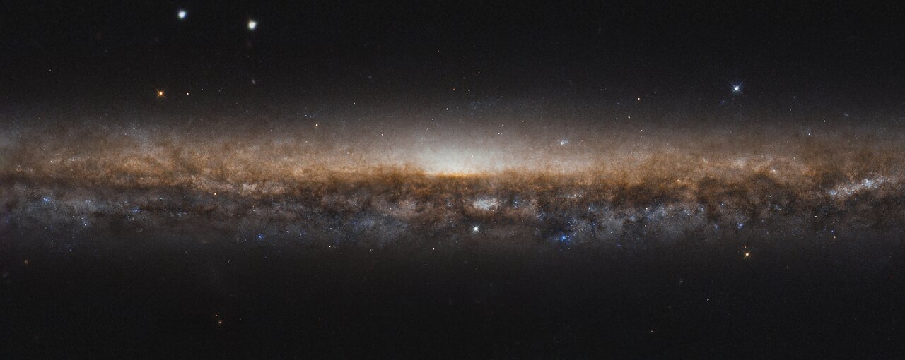 NGC 5907 é uma galáxia espiral, assim como a Via Láctea. Estendo-se por toda esta imagem como uma linha alongada de estrelas e poeira escura, seus belos braços espirais estão ocultos devido ao ângulo de visão a partir da Terra. Como a vemos de lado, é como se estivéssemos olhando para a borda de um prato. Por esse motivo, NGC 5907 também é conhecida como Galáxia da Lâmina da Faca, ficando a cerca de 50 milhões de anos-luz distância, na direção da boreal Constelação de Draco