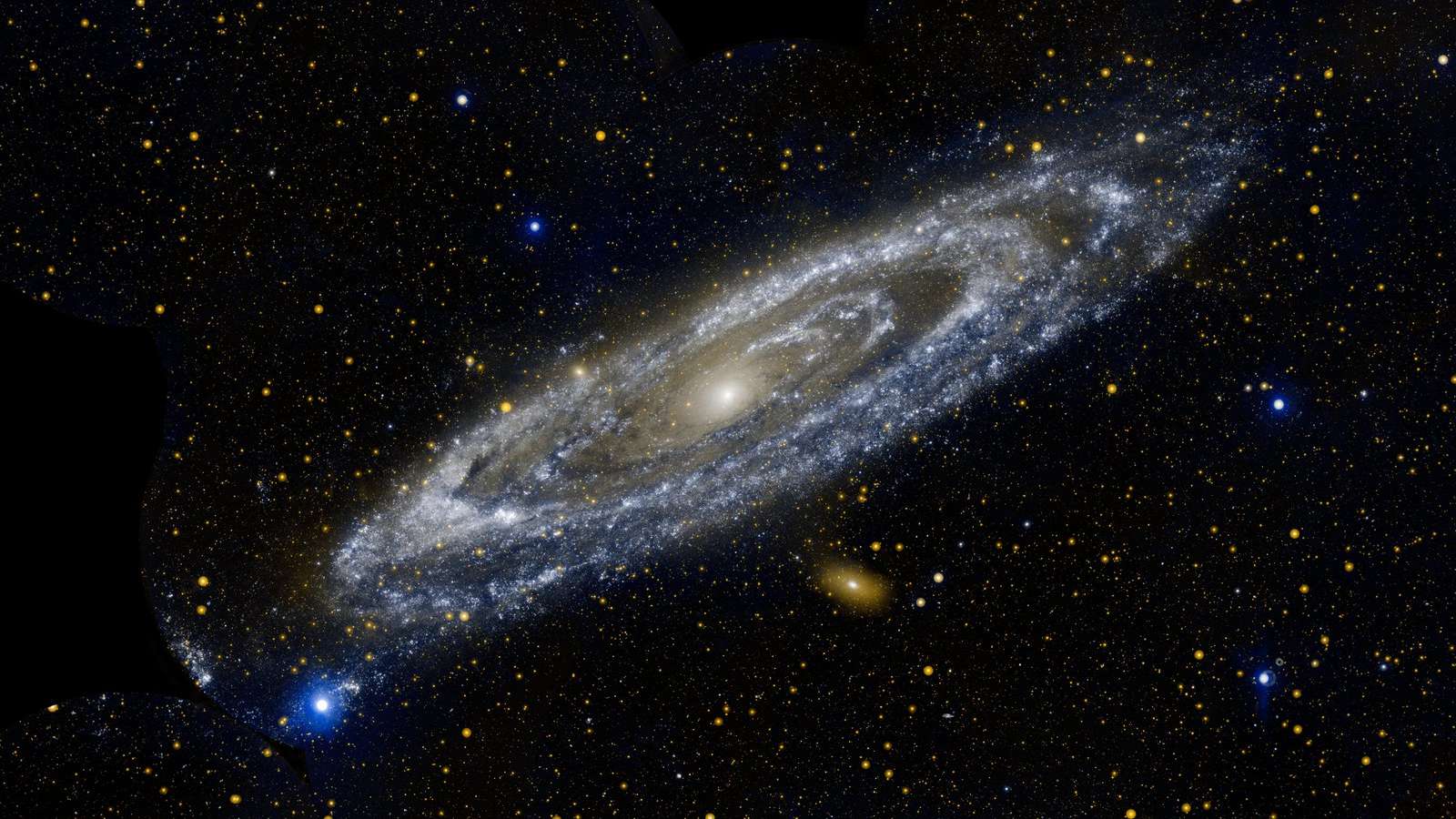 Estrelas quentes brilham intensamente nesta imagem, mostrando as emissões em ultravioleta de um objeto bem familiar. A aproximadamente 2,5 milhões de anos-luz de distância, a Galáxia de Andrômeda (M31) é a maior vizinha da nossa Via Láctea. Localizada na Constelação de Andrômeda, ela tem uma extensão de cerca de 260 mil anos-luz de diâmetro As faixas azul-esbranquiçadas da galáxia abrigam estrelas quentes, jovens e massivas. Faixas azul-acinzentadas traçam regiões onde a formação de estrelas está atualmente ocorrendo em densos casulos nublados. Já a bola central laranja-esbranquiçada revela uma congregação de estrelas antigas e mais frias, que se formaram há muito tempo