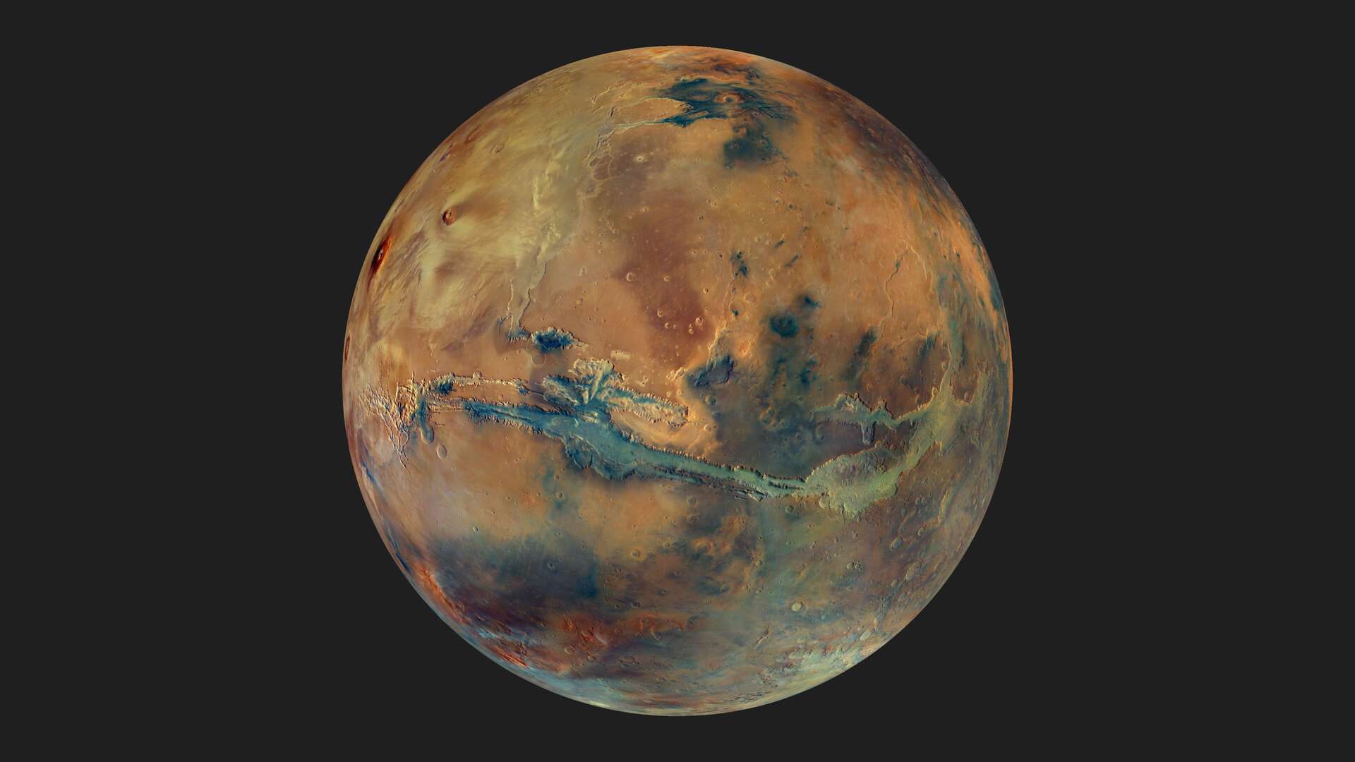 Nesta rica imagem de Marte, o mosaico revela a cor e a composição da superfície do planeta com detalhes espetaculares. Esta é a vista simulada a partir de um ponto de vista 2,5 mil km acima do colossal sistema de desfiladeiros chamado de Valles Marineris. As áreas em tons mais escuros de cinza representam areias basálticas preto-acinzentadas de origem vulcânica. Já as manchas mais claras mostram minerais argilosos e sulfatos. A grande cicatriz na face do planeta mostra a extensão dos Valles Marineris
