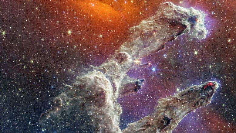 Ao combinar imagens dos icónicos Pilares da Criação obtidas por duas câmaras a bordo do Telescópio Espacial James Webb, novos detalhes dessa região de formação estelar foram revelados. Milhares de estrelas recém-formadas aparecem como esferas laranja brilhantes que ficam fora dos pilares de poeira. As regiões mais densas de poeira são moldadas em tons índigo, obscurecendo a visão das atividades dentro dos pilares . A poeira é um ingrediente importante na formação de estrelas. Quando nós de gás e poeira com massa suficiente se formam nos pilares, eles começam a entrar em colapso por conta de sua própria atração gravitacional, aumentando sua temperatura e formando novas estrelas. Os Pilares da Criação são parte da Nebulosa da Águia (NGC 6611) e ficam a cerca de 6,5 mil anos-luz de distância, na Constelação de Serpens (“A Serpente”)
