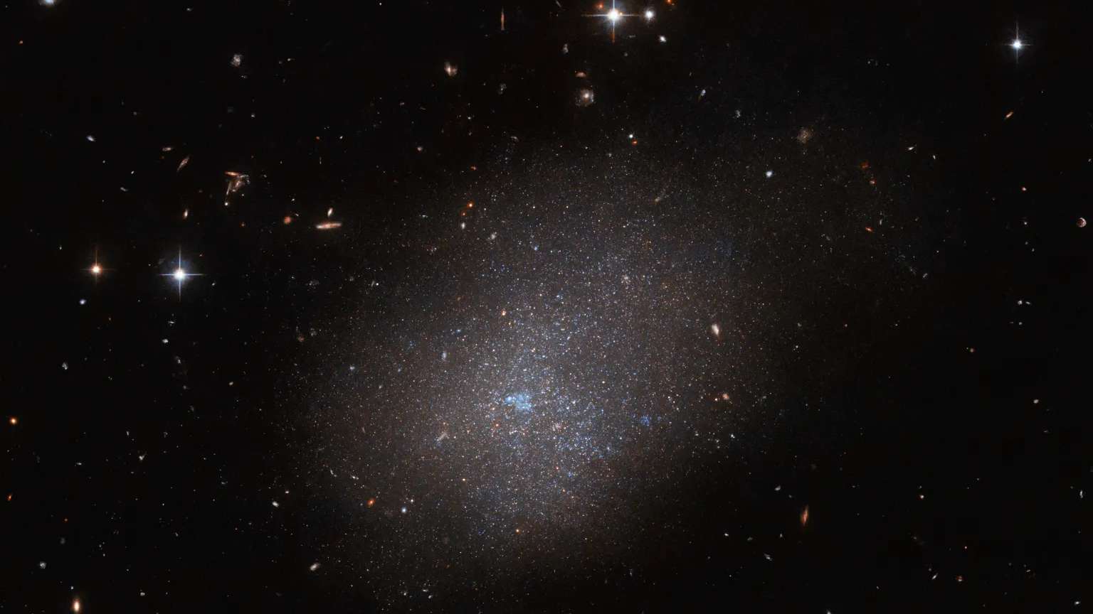 A galáxia ESO 300-16 é o destaque desta imagem do Telescópio Espacial Hubble. Esta galáxia, que fica a 28,7 milhões de anos-luz da Terra, na Constelação de Eridanus, é um conjunto de estrelas que se assemelha a uma nuvem cintilante. Outras galáxias distantes e estrelas em primeiro plano completam a imagem. Devido à sua forma indefinida, a ausência de um bulbo central ou braços espirais, ESO 300-16 é classificada como uma galáxia irregular. Nela, há muitas estrelas, mas todas estão amontoadas