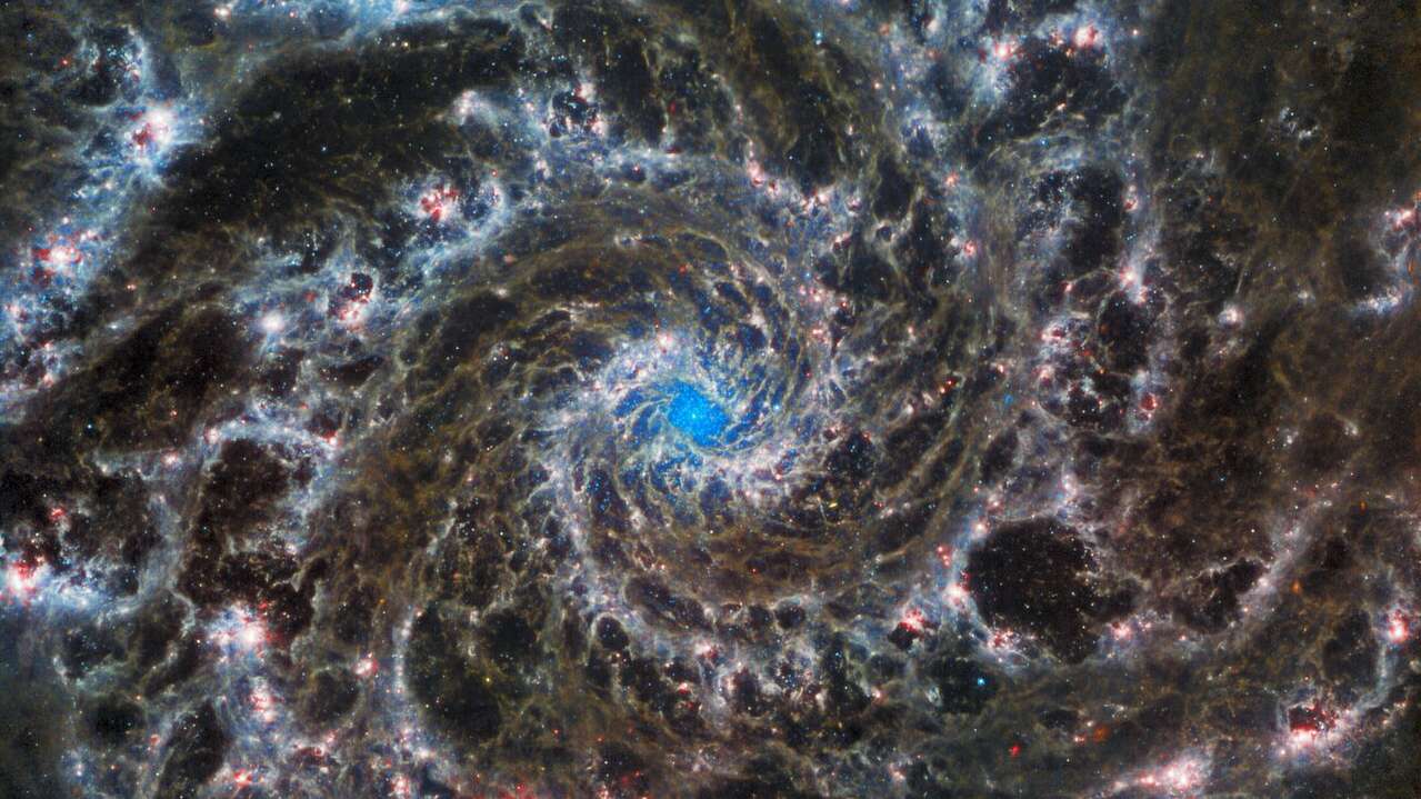 Esta imagem do Telescópio Espacial James Webb mostra o coração de M74, que também é conhecida como Galáxia Fantasma. A visão nítida revela delicados filamentos de gás e poeira nos grandiosos braços espirais que serpenteiam para fora do centro. A falta de gás na região nuclear também proporciona uma visão desobstruída do aglomerado de estrelas nucleares no centro da galáxia. M74 pertence a uma classe particular de galáxias espirais conhecidas como “grande design”, o que significa que os seus braços espirais são proeminentes e bem definidos. A Galáxia Fantasma está a cerca de 32 milhões de anos-luz de distância da Terra, na Constelação de Peixes