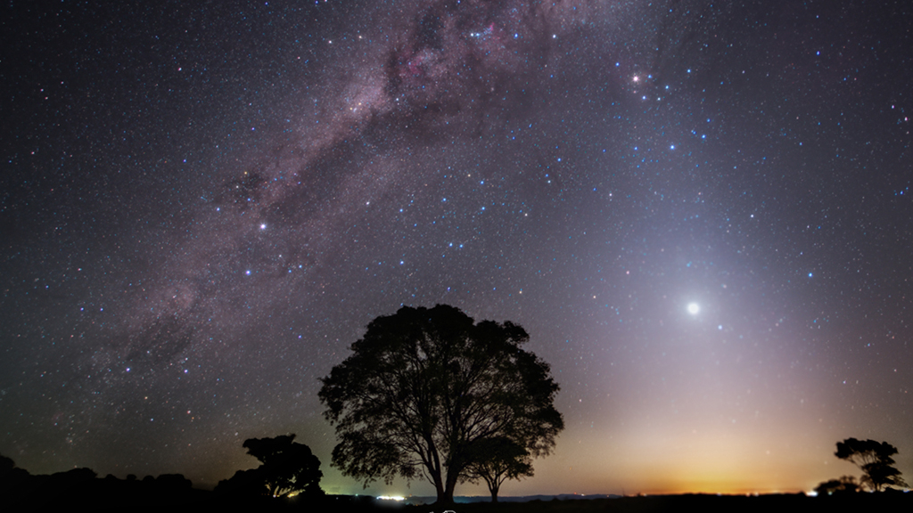 No céu brilhando em sua fase como estrela vespertina, Vênus está perto do horizonte ocidental nesta paisagem noturna. O registro foi feito em setembro de 2021, em Cascavel, região Sul do Brasil. Visto logo após o pôr do sol, Vênus aparece imerso em um cone de luz zodiacal, com a luz solar espalhada pela poeira ao longo do plano eclíptico do Sistema Solar. Estendendo-se acima do pôr do sol nesta noite, a luz zodiacal alcança ricos campos estelares e imensas nuvens de poeira interestelar na região central da Via Láctea