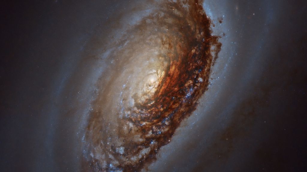 Messier 64 (M64) é uma galáxia espiral também conhecida como Galáxia do Olho Negro ou Galáxia da Bela Adormecida por conta da aparência que lembra pálpebras escuras. A sua região central está retratada nesta imagem. M64 fica a cerca de 17 milhões de anos-luz de distância, na Constelação de Coma Berenices. Nuvens de poeira obscurecem a região central, misturadas a aglomerados de jovens estrelas azuis e o brilho avermelhado do hidrogênio. M64 é composta por dois sistemas concêntricos e contra-rotativos. Enquanto as estrelas giram na mesma direção que o gás interestelar em sua região central, o gás nas regiões externas gira na direção oposta. Essas rotações incomuns são provavelmente resultado da fusão de duas galáxias, há bilhões de anos