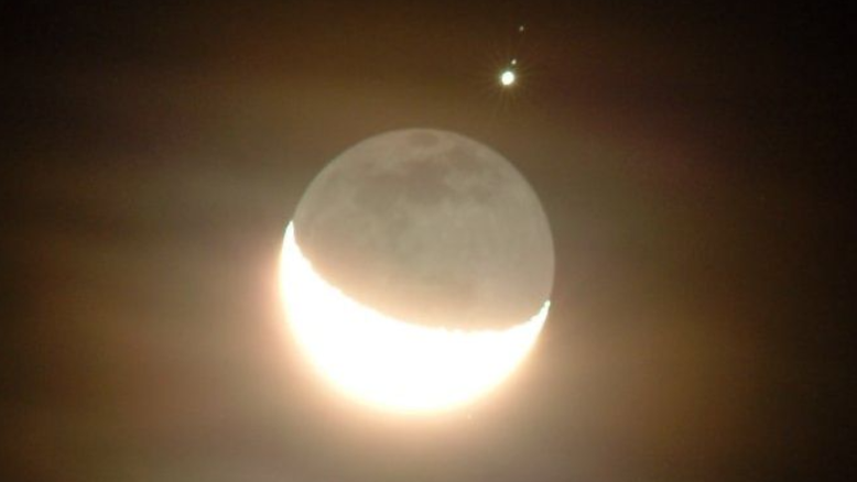 Em dezembro de 2004, em Colorado, nos EUA, a Lua Crescente brilhou ao lado do cintilante planeta Júpiter. Visto através de nuvens finas, o gigante gasoso do Sistema Solar aparece juntamente com dois de seus maiores satélites naturais, Ganimedes e Calisto, vistos como dois pequenos pontos de luz, de baixo para cima, na imagem. Além deles, Júpiter tem até o momento 95 satélites confirmados em sua órbita, que giram em volta dele da mesma forma como a Lua orbita a Terra 