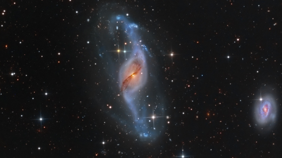 Esta imagem colorida revela um número surpreendente de galáxias próximas e distantes, na direção da Constelação da Ursa Maior. A mais impressionante é NGC 3718, a galáxia espiral deformada, próxima ao centro. Os braços espirais da NGC 3718 parecem retorcidos e estendidos, salpicados de jovens aglomerados de estrelas azuis. Longas faixas de poeira obscurecem suas regiões centrais amareladas. A apenas 150 mil anos-luz, à direita, está outra grande galáxia espiral, NGC 3729. As duas provavelmente estão interagindo gravitacionalmente, o que explica a aparência peculiar de NGC 3718