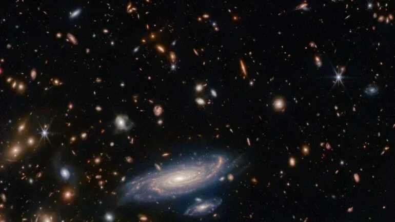 Um campo lotado de galáxias está retratado nesta imagem do Telescópio Espacial James Webb, junto a estrelas brilhantes exibindo picos de difração de seis pontas. A grande galáxia espiral centralizada foi batizada de LEDA 2046648 e está situada a pouco mais de um bilhão de anos-luz da Terra, na Constelação de Hércules. Um dos principais objetivos científicos do Webb é observar galáxias distantes e antigas para compreender os detalhes da sua formação, evolução e composição