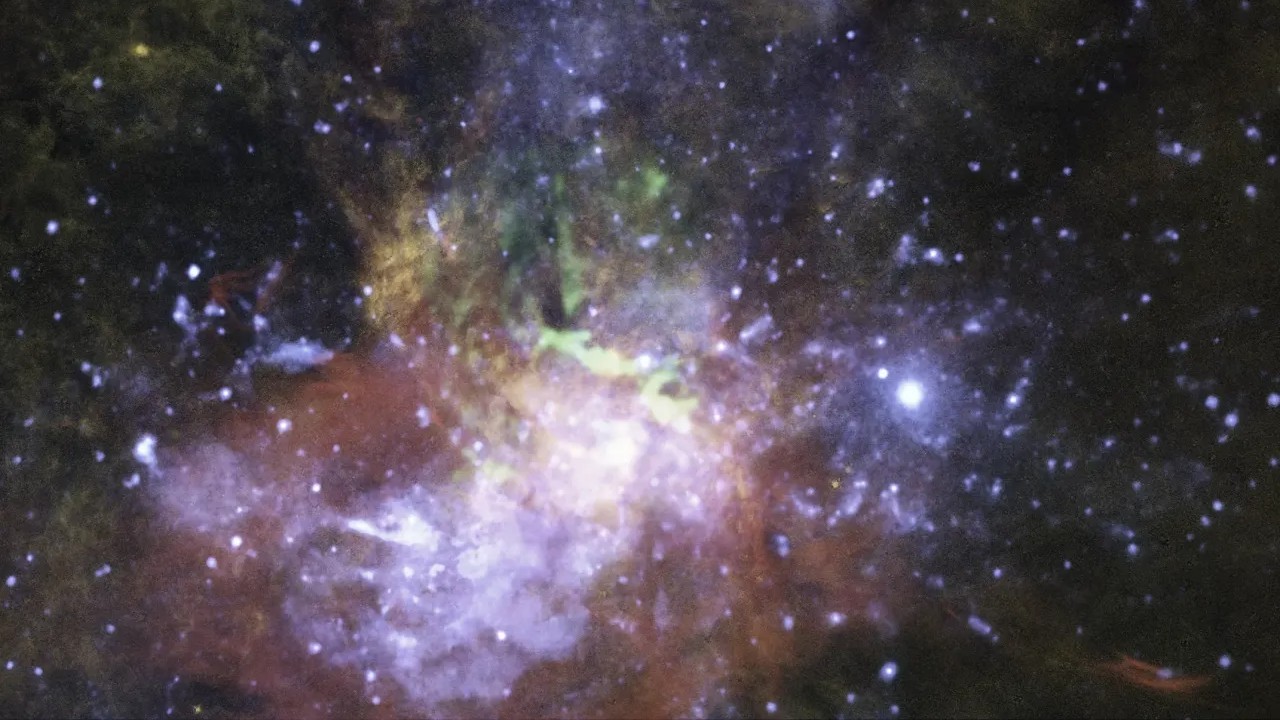Esta é uma visão composta de raios X, gás molecular e gás ionizado quente próximo ao centro galáctico na nossa Via Láctea, na direção da Constelação de Sagitário. As características de cor laranja são de gás hidrogênio brilhante. Perto do buraco negro, estão observações em raios X de gás superaquecido de cor azul e gás molecular em verde. Estes dados são evidências de que o buraco negro, localizado a cerca de 26 mil anos-luz de distância da Terra, acumula estrelas ou nuvens de gás e ejeta parte do material superaquecido ao longo do seu eixo de rotação