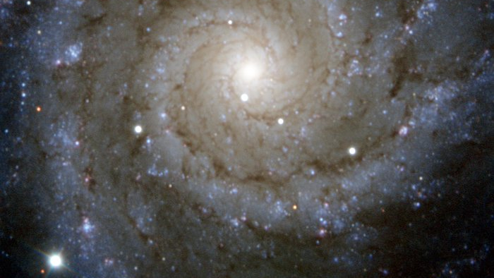 Esta imagem captada pelo PESSTO (Public ESO Spectroscopic Survey for Transient Objects), localizado no Observatório de La Silla, no Chile, mostra a galáxia espiral Messier 74. Nela, é possível notar a brilhante supernova do Tipo II, chamada SN2013ej, visível como a estrela mais brilhante na parte inferior esquerda. Essas supernovas ocorrem quando o núcleo de uma estrela massiva entra em colapso devido à sua própria gravidade, no final da sua vida. Este colapso resulta em uma explosão massiva que ejeta material para o espaço. Messier 74 fica a cerca de 30 milhões de anos-luz, na Constelação de Peixes