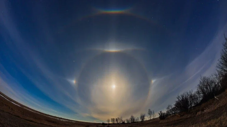 Uma Lua quase na fase Cheia, em abril de 2022, fez esta aparição luminosa para uma noite de primavera, no Norte de Alberta, no Canadá. O luar brilhante refratado e refletido por cristais de gelo hexagonais em nuvens altas criou um complexo de halos e arcos mais comumente vistos pela luz solar nos céus diurnos. Com Arcturus, a estrela Alfa da Constelação de Bootes (“O Boieiro”), à esquerda, e Regulus, a principal estrela da Constelação de Leão, à direita, a Lua está centrada em seu halo de 22 graus