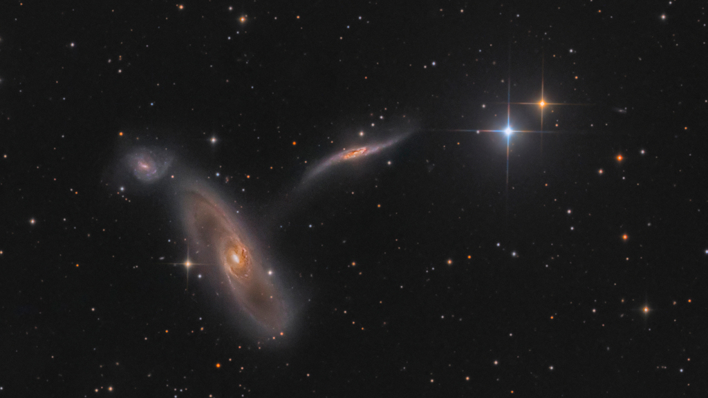 Este colorido campo de visão telescópico apresenta um trio de galáxias em interação a quase 90 milhões de anos-luz de distância, na direção da Constelação de Virgem. À direita, vê-se também duas estrelas pontiagudas da Via Láctea, em primeiro plano. Com braços espirais extensos e faixas de poeira, o membro dominante do trio, NGC 5566, é enorme, com cerca de 150 mil anos-luz de diâmetro. Logo acima dela fica a menor e azulada NGC 5569. Perto do centro, uma terceira galáxia, NGC 5560, é aparentemente esticada e distorcida por sua interação com a massiva NGC 5566