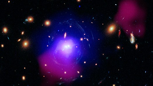 Nesta imagem, vê-se uma das mais poderosas erupções de um buraco negro, registrada no sistema conhecido como SDSS J1531+3414. A grande explosão, ocorrida há bilhões de anos, pode ajudar a explicar a formação de um padrão de aglomerados estelares em torno de duas galáxias massivas. SDSS J1531 é um enorme aglomerado de galáxias contendo centenas de galáxias individuais e enormes reservatórios de gás quente e matéria escura. No centro de SDSS J1531, localizado a cerca de 3,8 bilhões de anos-luz de distância, na direção da Constelação de Corona Borealis (“A Coroa do Norte”), observa-se duas das maiores galáxias do aglomerado em colisão