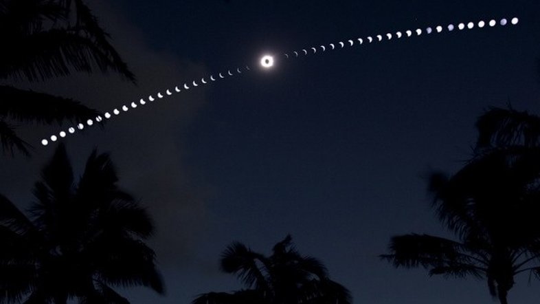 Enquanto a sombra da Lua Nova deslizava pelo Sul do Pacífico em 11 de julho de 2010, as pessoas se reuniram na praia de Anakena, no lado Norte da Ilha de Páscoa, para assistir ao Eclipse Solar Total. A experiência foi capturada nesta imagem composta, construída a partir de uma sequência de 50 exposições consecutivas. Ao centro, está o Sol totalmente eclipsado, rodeado pela coroa solar cintilante. As palmeiras aparecem em silhueta contra o céu escurecido e a tênue luz refletida na água. A Ilha de Páscoa - famosa pelas misteriosas estátuas Moai - recebeu este nome, pois foi descoberta pelo almirante holandês Jacob Roggeveen, no Domingo de Páscoa do ano de 1722