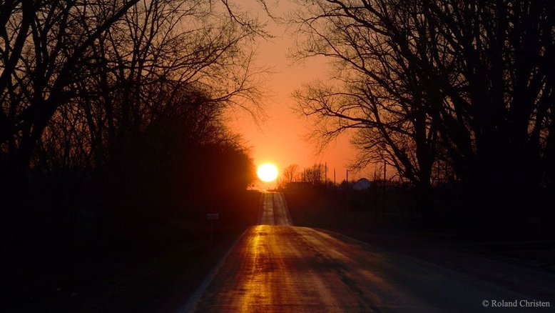 O que é isso no final da estrada? O Sol! O registro foi feito em um dos dois dias que há no ano no qual a Terra experimenta o fenômeno astronômico conhecido como Equinócio. Mais do que o momento no qual dia e noite são iguais (e daí vem o nome que resulta da junção do prefixo "aequus" e do sufixo "nox"), é também o momento em que o Sol nasce precisamente a Leste e se põe exatamente a Oeste. A estrada retratada fica no noroeste de Illinois, nos EUA, e avança de Leste a Oeste. A foto retrata o Equinócio Vernal, em março de 2015. Interpretado simbolicamente em muitas culturas, o fenômeno astronômico do equinócio de março é considerado o primeiro dia da primavera, no Hemisfério Norte, e do outono, no Hemisfério Sul