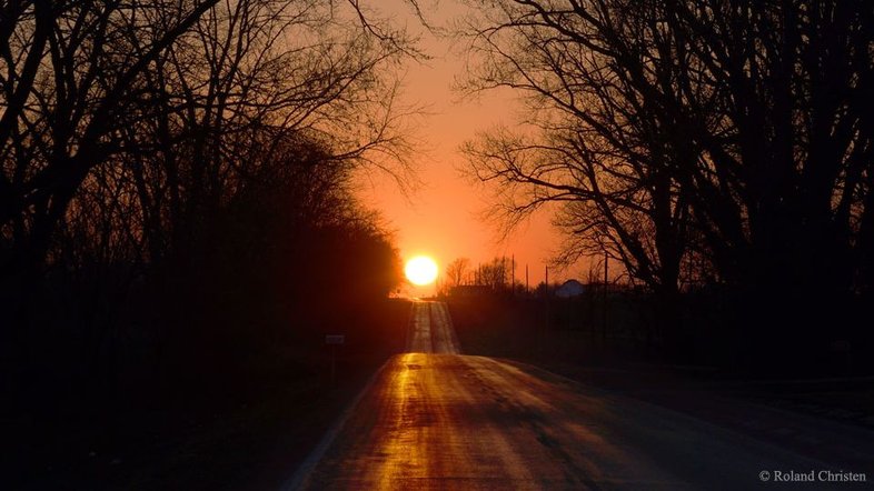 O que é isso no final da estrada? O Sol! O registro foi feito em um dos dois dias que há no ano no qual a Terra experimenta o fenômeno astronômico conhecido como Equinócio. Mais do que o momento no qual dia e noite são iguais (e daí vem o nome que resulta da junção do prefixo "aequus" e do sufixo "nox"), é também o momento em que o Sol nasce precisamente a Leste e se põe exatamente a Oeste. A estrada retratada fica no noroeste de Illinois, nos EUA, e avança de Leste a Oeste. A foto retrata o Equinócio Vernal, em março de 2015. Interpretado simbolicamente em muitas culturas, o fenômeno astronômico do equinócio de março é considerado o primeiro dia da primavera, no Hemisfério Norte, e do outono, no Hemisfério Sul