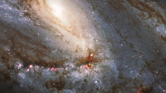 O Hubble capturou esta vista espetacular da maior entre as galáxias do Trio do Leão, que tem uma anatomia incomum: ela exibe braços espirais assimétricos e um núcleo aparentemente deslocado. A anatomia peculiar é provavelmente causada pela atração gravitacional dos outros dois membros do trio. A incomum galáxia espiral, chamada de Messier 66, está localizada a uma distância de cerca de 35 milhões de anos-luz, na direção da Constelação de Leão. Juntamente com Messier 65 e NGC 3628, Messier 66 forma um trio de galáxias espirais em interação