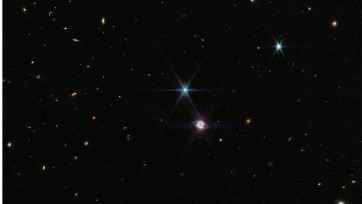 Nesta imagem captada pelo Telescópio Espacial James Webb, vê-se algumas centenas de galáxias de fundo ao lado do sistema formado pelo planeta Netuno e seus 14 satélites naturais. Além do gigante gasoso, retratado com os seus anéis, domina a imagem um ponto de luz muito brilhante, com picos de difração, que não é uma estrela, mas a maior de suas luas, Tritão. Netuno, quando comparado à Terra, é um planeta gigante. Se a Terra fosse do tamanho de uma moeda de cinco centavos, Netuno seria tão grande quanto uma bola de basquete. No entanto, Netuno parece relativamente pequeno nesta visão de campo ampla de nosso vasto universo
