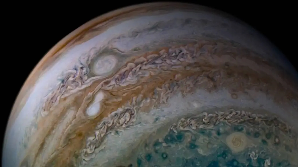 Esta imagem da atmosfera de Júpiter obtida pela sonda Juno inclui algo notável: duas tempestades flagradas em processo de fusão. As duas formas ovais brancas, vistas na faixa laranja à esquerda, são tempestades anticiclônicas - isto é, tempestades que giram no sentido anti-horário. A maior das duas formas ovais tem sido rastreada há muitos anos e vinha crescendo por meio de fusões com outras formas ovais brancas anticiclônicas. O registro conseguiu capturar esta nova fusão, que normalmente ocorre em apenas alguns dias