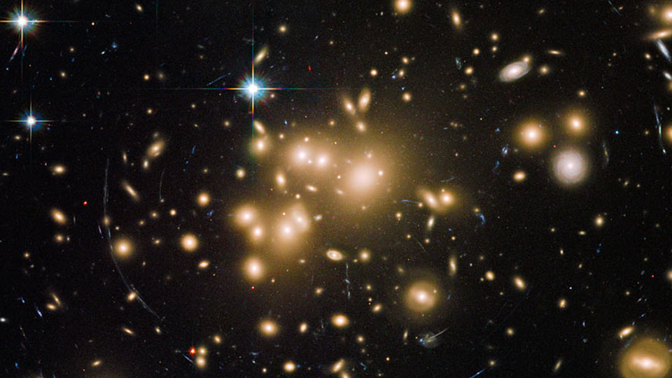 Este é um dos objetos mais massivos do universo visível. Abell 1689 é um aglomerado de galáxias, cuja capacidade para deformar o espaço demonstra o previsto pela teoria da relatividade, de Albert Einstein. O desvio da luz de galáxias atrás do aglomerado produz múltiplas imagens curvas. O poder desta enorme lente gravitacional depende da sua massa, mas a matéria visível - as galáxias amareladas - representa apenas 1% da massa necessária para produzir as imagens azuladas e deformadas das galáxias de fundo. A maior parte de sua massa está na forma da ainda misteriosa matéria escura. Abell 1689 está localizado a cerca de 2,2 bilhões de anos luz de distância, na Constelação de Virgem