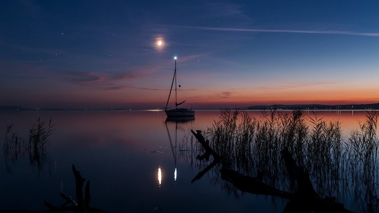O planeta Marte, a Lua e Saturno brilham neste céu sereno. A luz dourada do Sol ainda está espalhada ao longo do horizonte, capturada após o pôr do Sol, em setembro de 2014. A reunião noturna de planetas errantes e da Lua foi apreciada no planeta Terra. Nesta foto, que registra as águas calmas do Lago Balaton, na Hungria, eles foram acompanhados pela luz do mastro do veleiro. A luz do mastro, os planetas e a Lua estão todos posando perto do plano da eclíptica