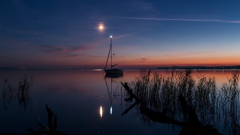 O planeta Marte, a Lua e Saturno brilham neste céu sereno. A luz dourada do Sol ainda está espalhada ao longo do horizonte, capturada após o pôr do Sol, em setembro de 2014. A reunião noturna de planetas errantes e da Lua foi apreciada no planeta Terra. Nesta foto, que registra as águas calmas do Lago Balaton, na Hungria, eles foram acompanhados pela luz do mastro do veleiro. A luz do mastro, os planetas e a Lua estão todos posando perto do plano da eclíptica