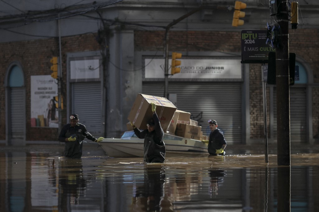 Homens carregam e transportam pacotes ao longo de uma rua inundada no centro histórico da cidade de Porto Alegre (RS)