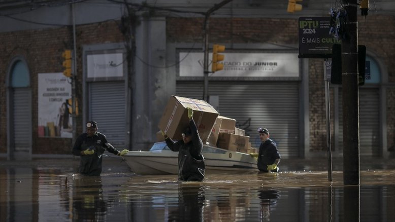 Homens carregam e transportam pacotes ao longo de uma rua inundada no centro histórico da cidade de Porto Alegre (RS)