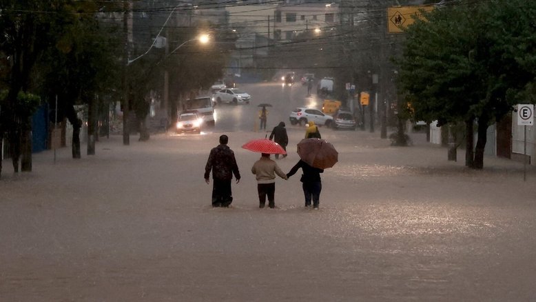 Pessoas caminham de guarda-chuva em rua inundada de Porto Alegre (RS)