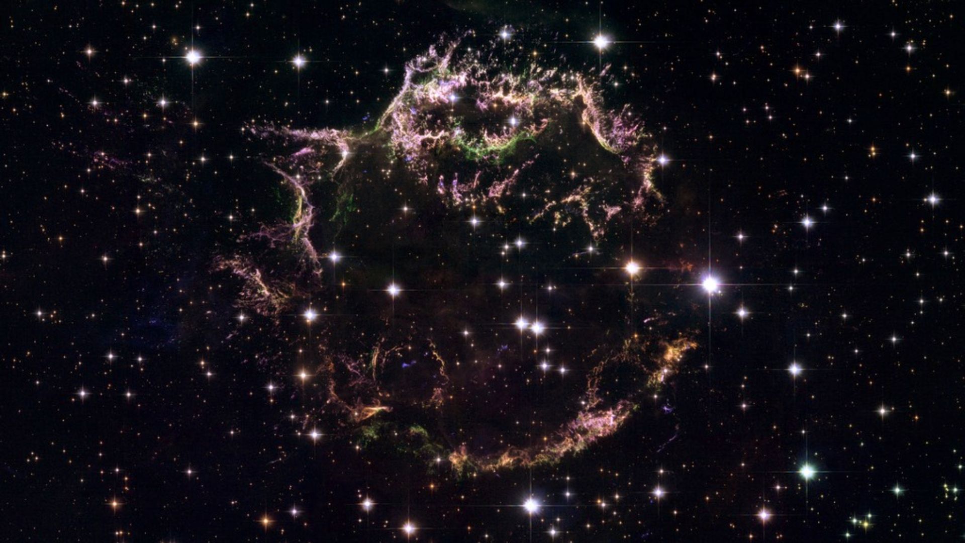 Cassiopeia A (Cas A) exibe os Cassiopeia A (Cas A) exibe os remanescentes da explosão de uma supernova, localizada a cerca de onze mil anos-luz de distância, na Constelação de Cassiopeia. Trata-se do remanescente de supernova mais jovem, com cerca de 340 anos, conhecido na Via Láctea. Sua estrutura complexa revela os fragmentos despedaçados de uma estrela, com uma espécie de anel quebrado de material estelar ejetado. Os redemoinhos de detritos brilham com o calor das ondas de choque da explosão. As cores indicam diferenças na composição química. Os filamentos verdes são ricos em oxigênio, os vermelhos e roxos são enxofre, e os azuis são compostos principalmente de hidrogênio e nitrogênio. Uma supernova como Cas A é o fim explosivo de uma estrela massiva que entra em colapso sob o peso da sua própria gravidade
