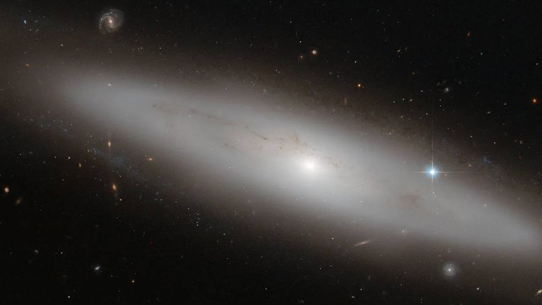 A Constelação de Virgem é a maior do zodíaco. Sua característica mais atraente, entretanto, é o grande número de galáxias que existem dentro dela. Nesta imagem, entre uma multidão de galáxias espirais, elípticas e irregulares - vistas de face e de lado -, está NGC 4866, uma galáxia lenticular situada a cerca de 80 milhões de anos-luz da Terra. Nela, podemos apreciar o seu brilhante bojo central, que contém principalmente estrelas antigas. A galáxia é observada da Terra quase de lado, deixando sua estrutura de disco claramente visível. À direita, vê-se uma estrela muito brilhante, que parece estar dentro de NGC 4866. No entanto, na verdade, esta estrela está muito mais perto em nossa linha a visão, a partir da Via Láctea