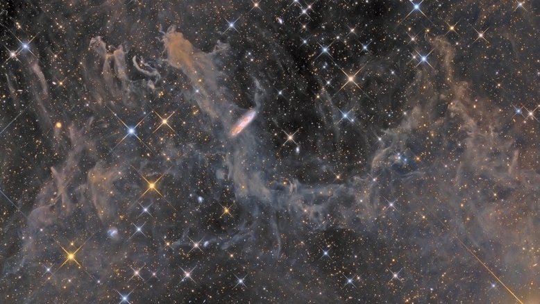 Estrelas pontiagudas e formas inusitadas abundam nesta profunda paisagem cósmica, na direção da Constelação do Pégaso. As estrelas mais brilhantes apresentam picos de difração. A nuvem difusa catalogada como MBM 54, localizada a menos de mil anos-luz de distância, preenche a cena. Outras galáxias, muito além da Via Láctea, estão visíveis, incluindo a impressionante galáxia espiral NGC 7497, a cerca de 60 milhões de anos-luz de distância. Vistos quase de lado, perto do centro do campo, os braços espirais e as faixas de poeira de NGC 7497 ecoam as cores das estrelas e da poeira da Via Láctea