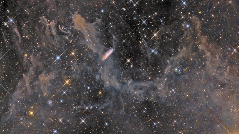 Estrelas pontiagudas e formas inusitadas abundam nesta profunda paisagem cósmica, na direção da Constelação do Pégaso. As estrelas mais brilhantes apresentam picos de difração. A nuvem difusa catalogada como MBM 54, localizada a menos de mil anos-luz de distância, preenche a cena. Outras galáxias, muito além da Via Láctea, estão visíveis, incluindo a impressionante galáxia espiral NGC 7497, a cerca de 60 milhões de anos-luz de distância. Vistos quase de lado, perto do centro do campo, os braços espirais e as faixas de poeira de NGC 7497 ecoam as cores das estrelas e da poeira da Via Láctea
