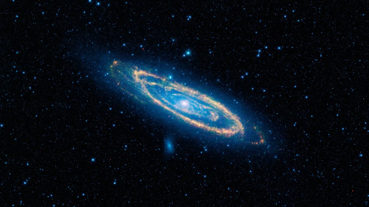 A imensa galáxia de Andrômeda, também conhecida como Messier 31 ou simplesmente M31, é o destaque desta imagem do Wide-field Infrared Survey Explorer (WISE), da NASA. O WISE usou todos os seus quatro detectores infravermelhos para captar esta imagem: a luz de 3,4 e 4,6 microns é azul; a luz de 12 microns é verde; e a luz de 22 microns é vermelha. O azul destaca estrelas maduras, enquanto o amarelo e o vermelho mostram a poeira aquecida por estrelas massivas recém-nascidas. A galáxia de Andrômeda fica a cerca de 2,5 milhões de anos-luz de distância, na direção da Constelação de Andrômeda 
