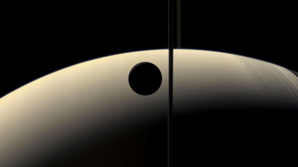 Tons suaves, orbes parcialmente iluminados, um traço fino do anel e sombras leves destacam esta visão discreta dos arredores majestosos do gigante planeta Saturno. Olhando quase para trás em direção ao Sol, a espaçonave robô Cassini capturou as fases crescentes de Saturno e de sua lua Reia. Como a espaçonave estava quase no plano dos anéis de Saturno, eles estão visíveis nesta imagem apenas como uma linha fina, ao centro