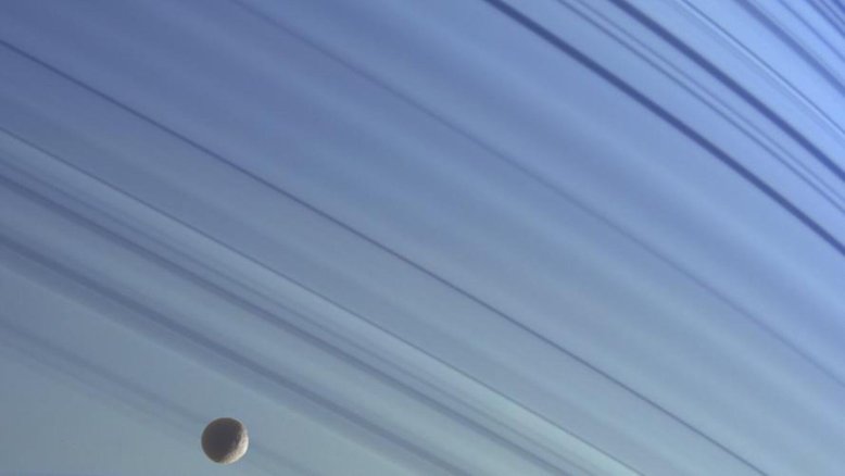 A pequena lua de Saturno, Mimas, flutua em sua órbita contra o pano de fundo azul das latitudes norte do planeta, nesta imagem em cores reais obtida pela espaçonave Cassini. As crateras deste gelado satélite natural de Saturno, que tem apenas 398 quilômetros de diâmetro, o dão uma aparência ondulada. As imagens foram obtidas em janeiro de 2005, a uma distância de aproximadamente 1,4 milhão de quilômetros de Saturno. Imagens com filtros espectrais infravermelho, verde e ultravioleta foram combinadas e as cores foram ajustadas para refletir com a aparência da cena em cores naturais