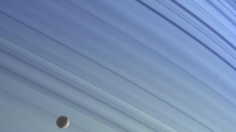 A pequena lua de Saturno, Mimas, flutua em sua órbita contra o pano de fundo azul das latitudes norte do planeta, nesta imagem em cores reais obtida pela espaçonave Cassini. As crateras deste gelado satélite natural de Saturno, que tem apenas 398 quilômetros de diâmetro, o dão uma aparência ondulada. As imagens foram obtidas em janeiro de 2005, a uma distância de aproximadamente 1,4 milhão de quilômetros de Saturno. Imagens com filtros espectrais infravermelho, verde e ultravioleta foram combinadas e as cores foram ajustadas para refletir com a aparência da cena em cores naturais
