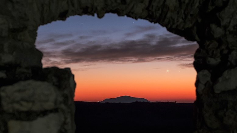 Os planetas internos, Vênus e Mercúrio, nunca se afastam do Sol e, por esse motivo, estão sempre visíveis por pouco tempo, no céu da Terra. Nesta imagem, os dois estão reunidos, perto do horizonte Oeste, logo após o pôr do Sol, em uma conjunção. A dupla está enquadrada nesta visão do céu, feita em janeiro de 2015, nas ruínas do Castelo Szarvasko, na Hungria. Acima da silhueta vulcânica, Vênus é o ponto mais brilhante, separado de Mercúrio, que está mais à direita