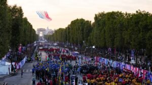 A equipe de vôo acrobático de elite da Força Aérea Francesa "Patrouille de France" se apresenta enquanto membros da delegação chegam à avenida Champs-Elysees com o Arco do Triunfo ao fundo, durante a Cerimônia de Abertura dos Jogos Paraolímpicos de Paris 2024, em Paris, em 28 de agosto de 2024. Dimitar DILKOFF/AFP