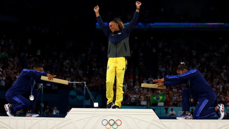 A medalhista de ouro Rebeca Andrade do Brasil comemora no pódio com a medalhista de prata Simone Biles dos Estados Unidos e o medalhista de bronze Jordan Chiles dos Estados Unidos